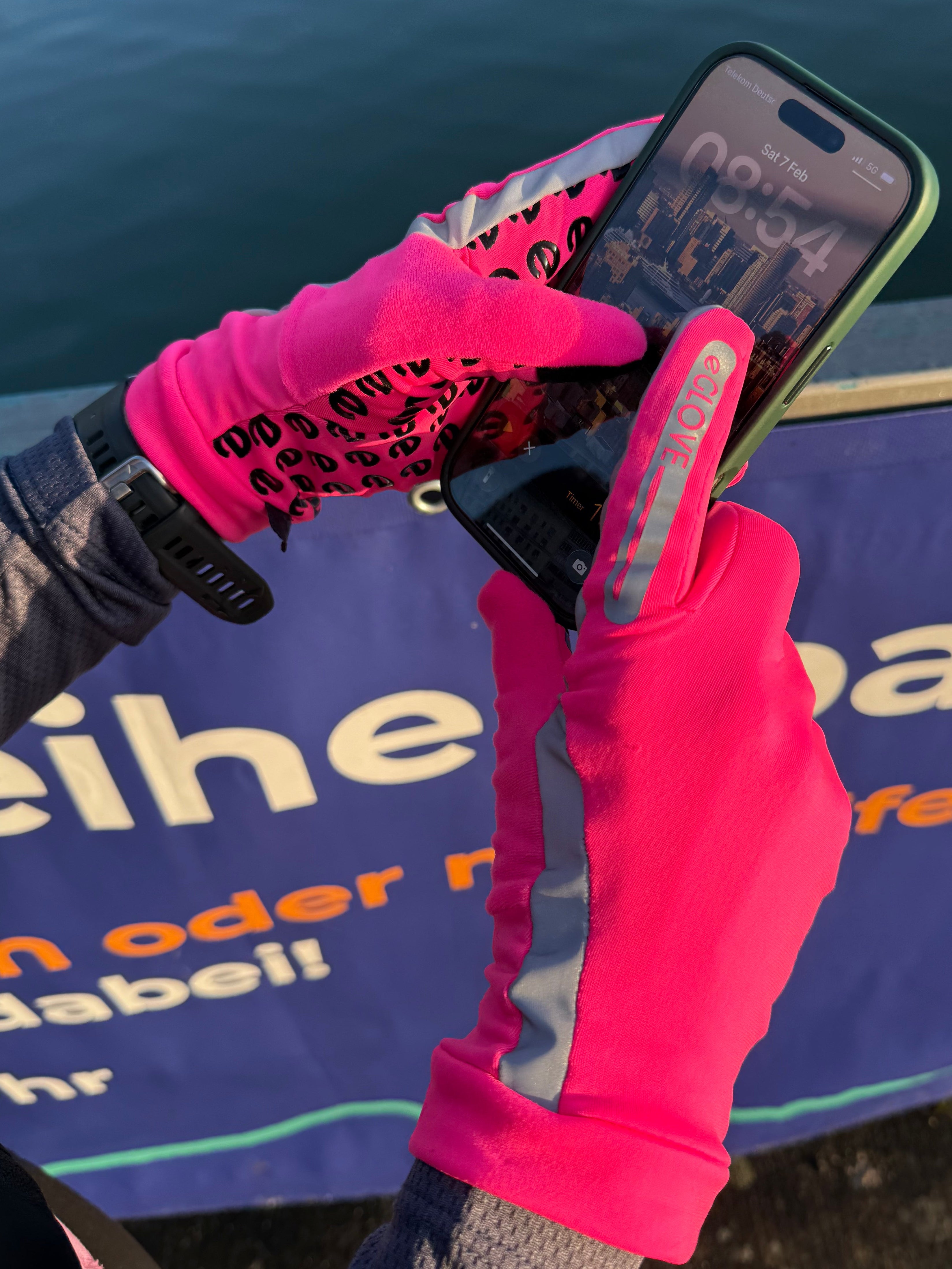 Person using a smartphone with touchscreen pink running gloves by a lake
