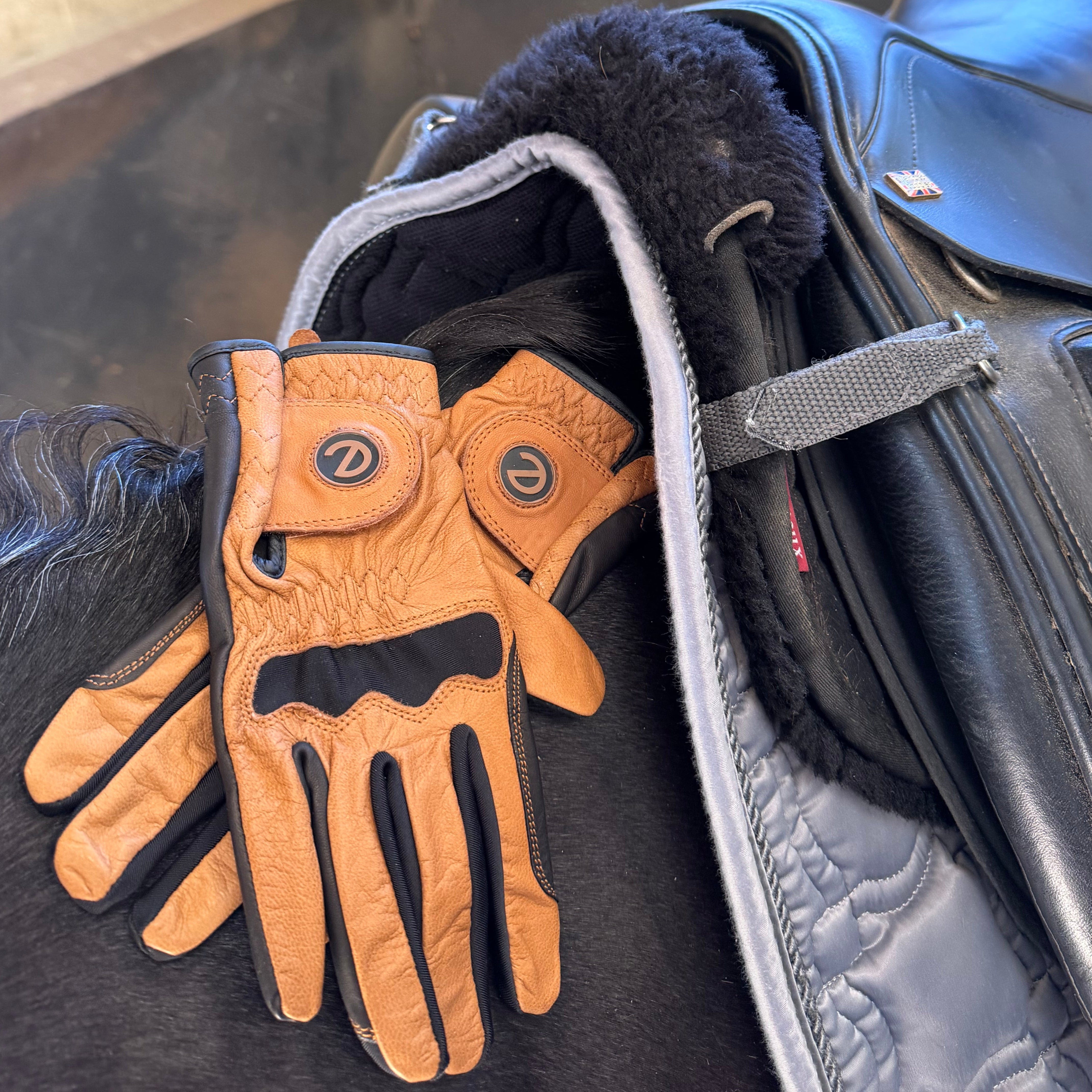 Brown leather glove on a horse's bridle with a saddle in the background.